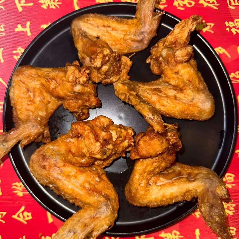 Crispy fried chicken wings on a black plate, set against a vibrant red and gold patterned tablecloth.